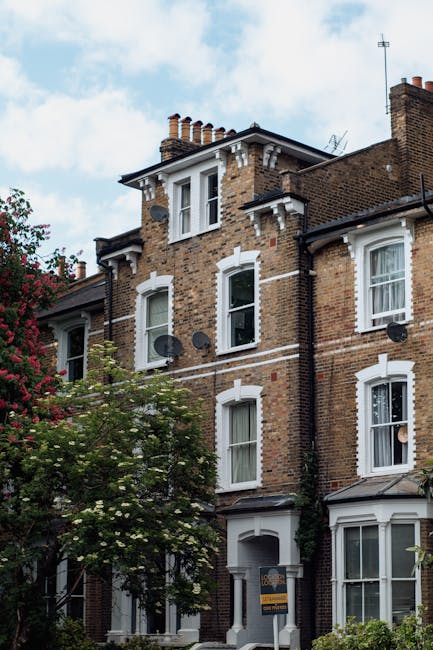 Photograph of a three-storey Victorian-style house with a brick facade and white decorative window frames, situated on a residential street. The ground floor features a white front door with a small w